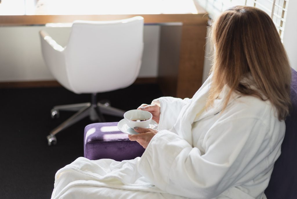 Woman in bathrobe sipping tea in luxury hotel room in morning